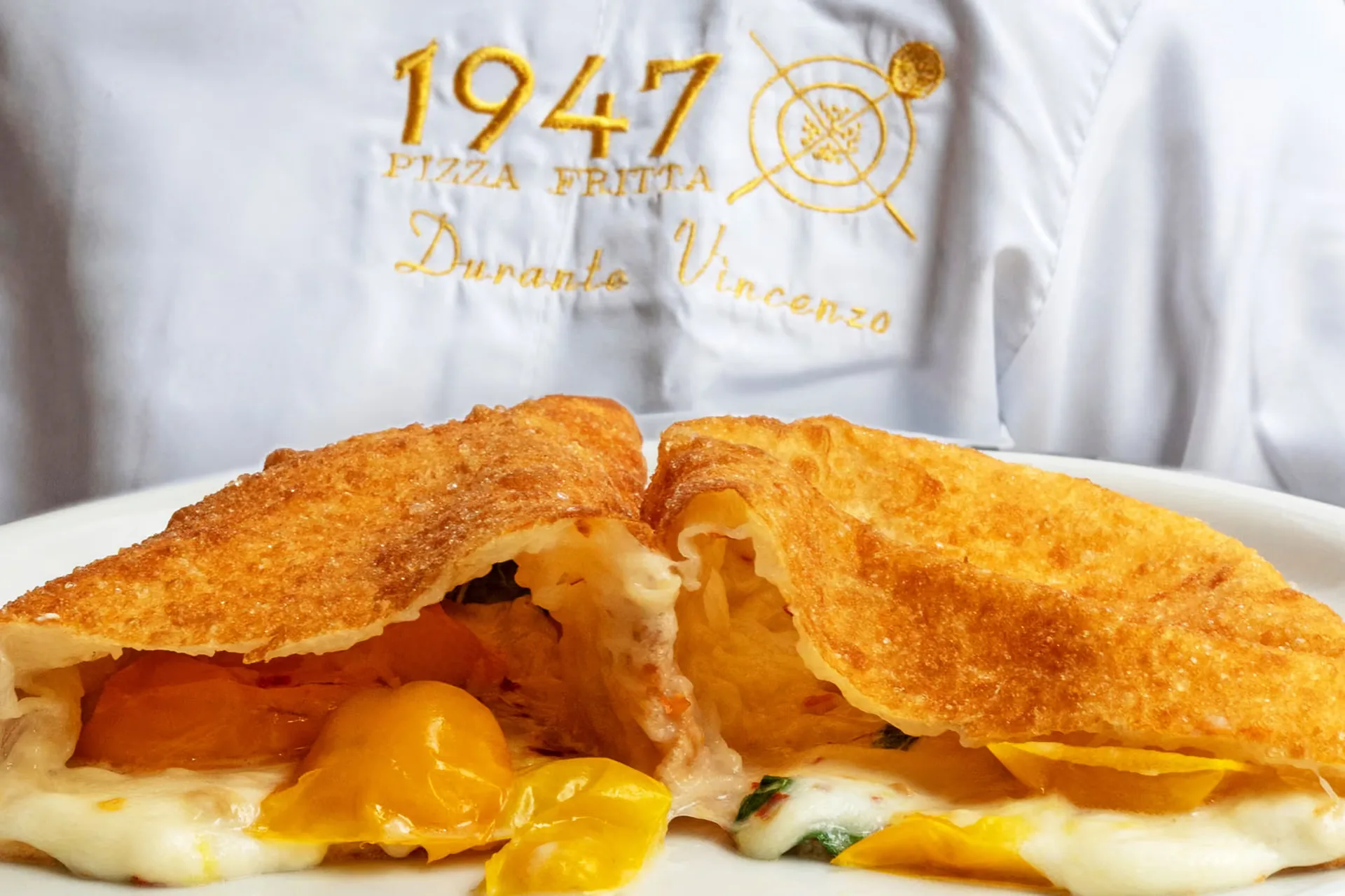 Pizza fritta ripiena di mozzarella e pomodorini gialli, con il grembiule ricamato 1947 Pizza Fritta: progetto 1947 Pizza Fritta di FV Digital Agency
